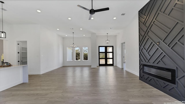 unfurnished living room featuring light wood finished floors, ceiling fan with notable chandelier, and recessed lighting