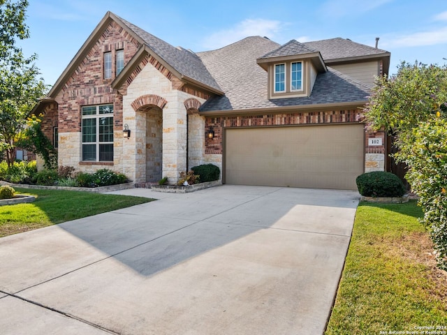 view of front of home with a shingled roof, an attached garage, a front yard, stone siding, and driveway