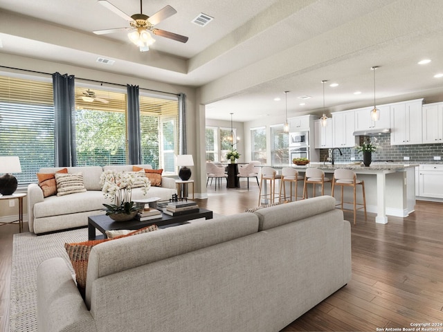 living area featuring a tray ceiling, dark wood-style flooring, recessed lighting, visible vents, and ceiling fan