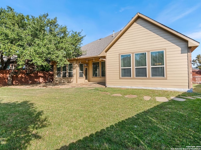 rear view of house featuring roof with shingles, a patio area, a lawn, and fence