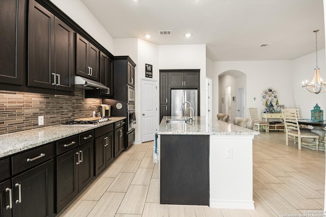 kitchen featuring arched walkways, under cabinet range hood, stainless steel appliances, a sink, and visible vents