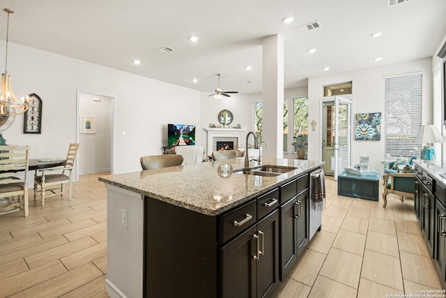 kitchen with a sink, visible vents, open floor plan, a lit fireplace, and an island with sink