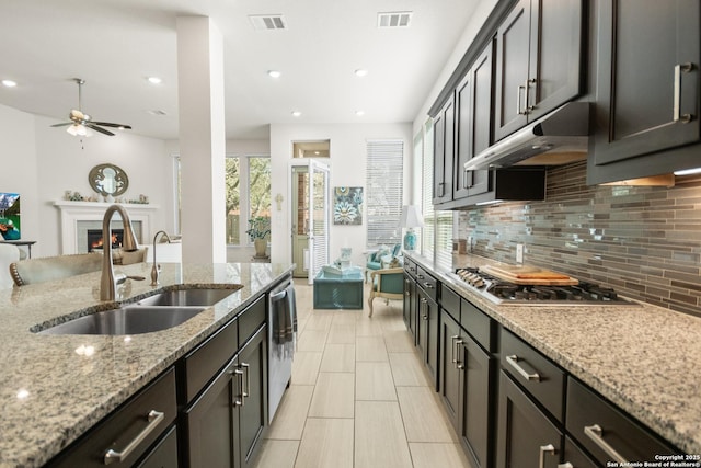 kitchen featuring a warm lit fireplace, visible vents, appliances with stainless steel finishes, under cabinet range hood, and a sink