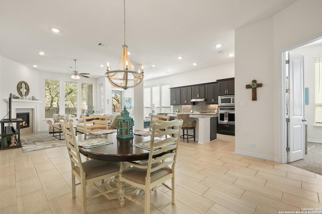 dining area with recessed lighting, a lit fireplace, baseboards, and ceiling fan with notable chandelier