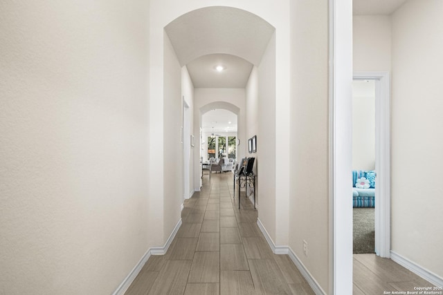 hallway featuring arched walkways, baseboards, and wood tiled floor