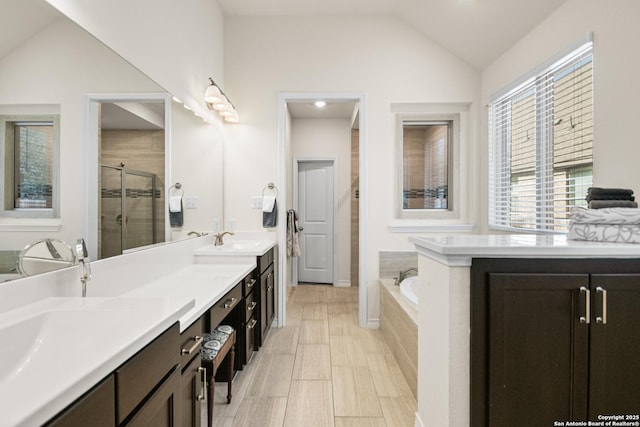 full bathroom featuring lofted ceiling, a garden tub, a sink, double vanity, and a stall shower