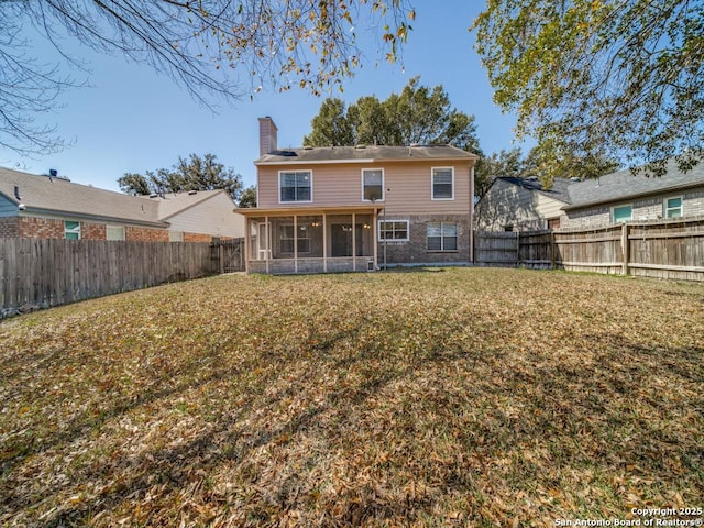 rear view of property with a sunroom, a fenced backyard, a chimney, and a yard