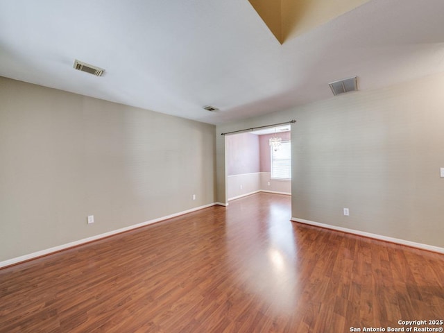 empty room with wood finished floors, visible vents, and baseboards