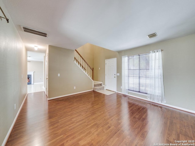 unfurnished living room featuring stairs, a lit fireplace, wood finished floors, and visible vents