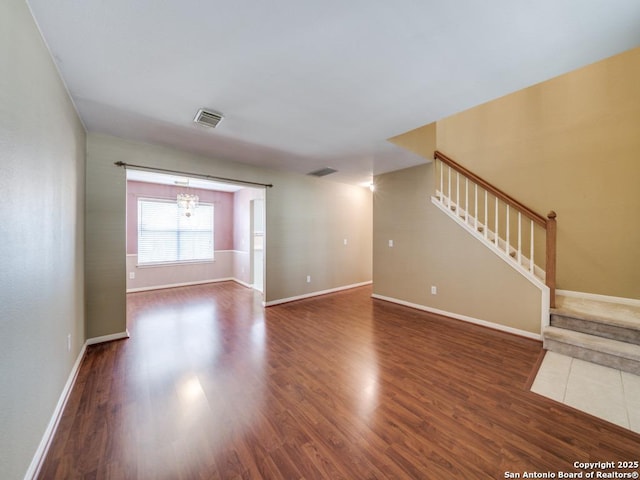 unfurnished living room featuring visible vents, stairway, baseboards, and wood finished floors