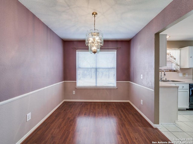 unfurnished dining area with a chandelier, baseboards, a sink, and light wood finished floors