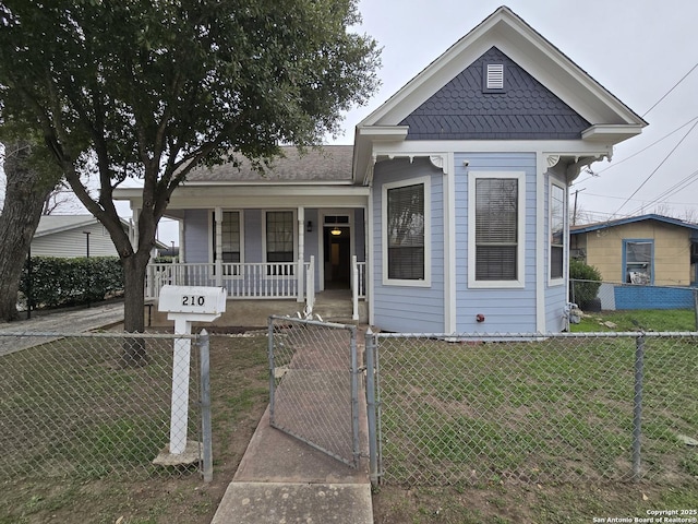 shotgun-style home featuring covered porch, a fenced front yard, a gate, and a front lawn