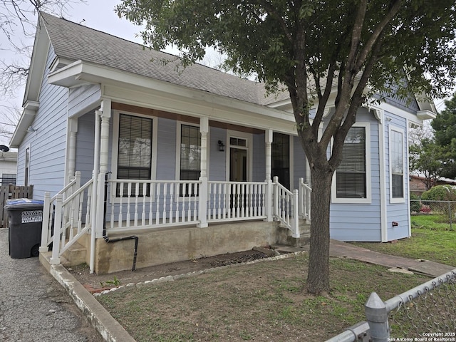 view of front of property featuring covered porch, fence, and roof with shingles