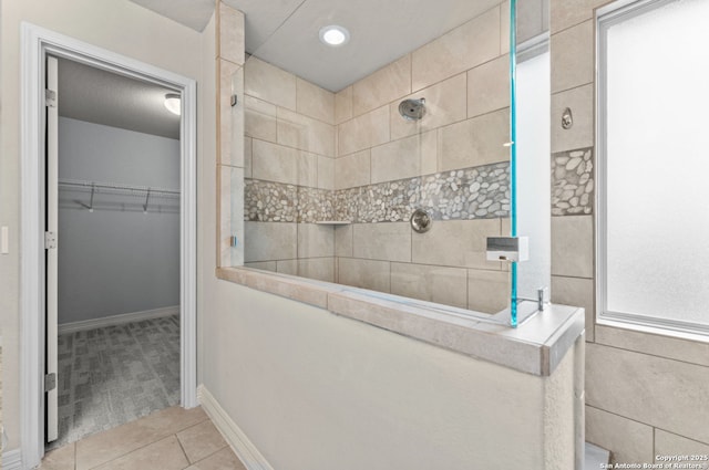 bathroom with a walk in closet, tile patterned flooring, baseboards, and a walk in shower