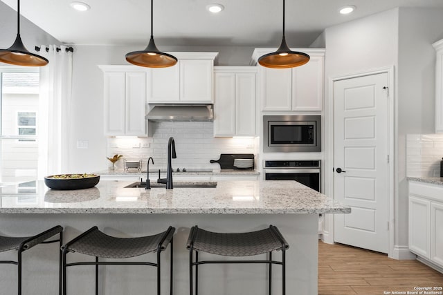 kitchen with a kitchen breakfast bar, stainless steel appliances, white cabinetry, and under cabinet range hood