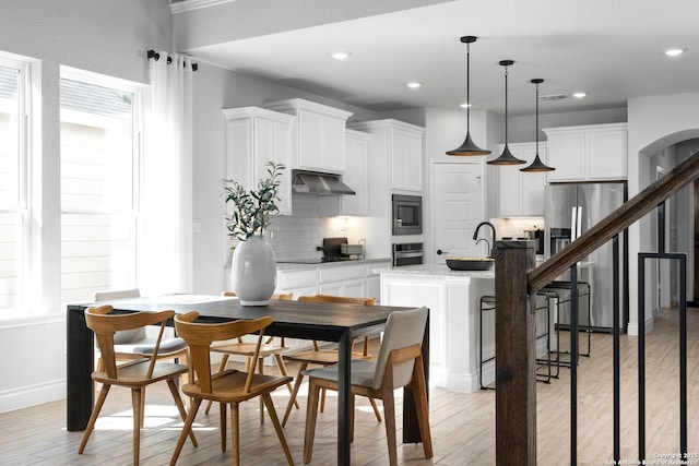 dining space featuring light wood finished floors, baseboards, visible vents, arched walkways, and recessed lighting