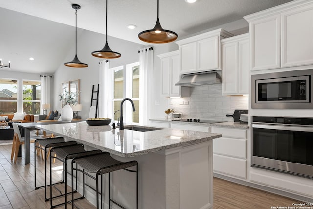 kitchen with stainless steel appliances, backsplash, white cabinetry, a sink, and under cabinet range hood