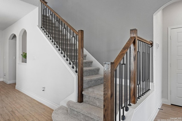 staircase featuring baseboards, arched walkways, and wood finished floors