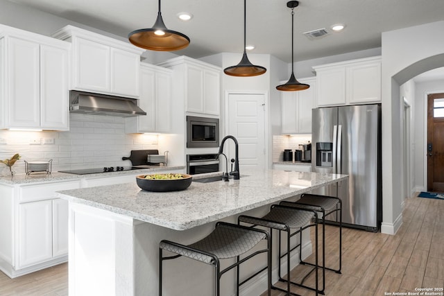 kitchen featuring arched walkways, under cabinet range hood, a sink, visible vents, and appliances with stainless steel finishes