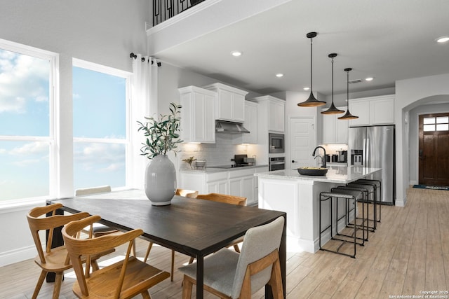 kitchen featuring arched walkways, under cabinet range hood, stainless steel appliances, light wood-style floors, and white cabinets