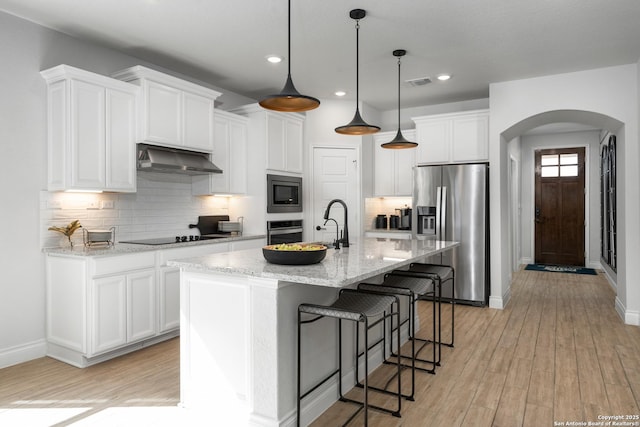 kitchen with arched walkways, stainless steel appliances, white cabinetry, light wood-type flooring, and under cabinet range hood