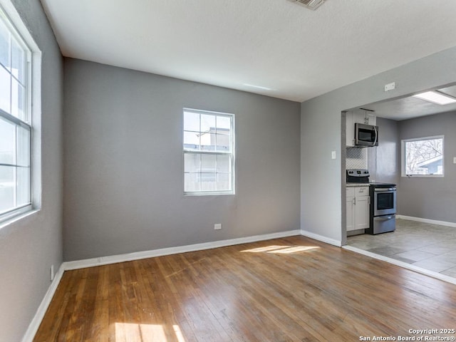 empty room with light wood-style floors, visible vents, and baseboards