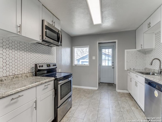 kitchen featuring baseboards, appliances with stainless steel finishes, a sink, and white cabinets