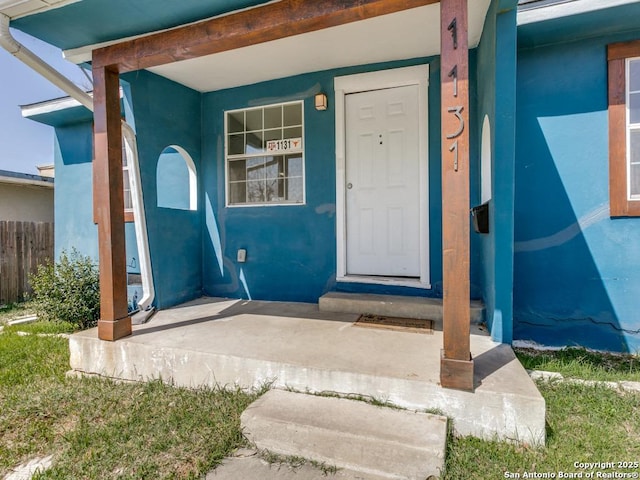 doorway to property featuring fence and stucco siding