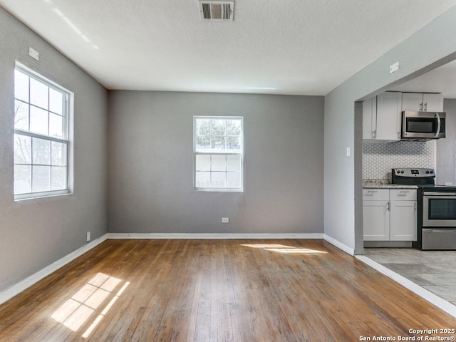 kitchen featuring light wood finished floors, tasteful backsplash, visible vents, baseboards, and appliances with stainless steel finishes