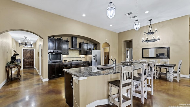 kitchen featuring wall chimney range hood, concrete floors, stainless steel appliances, and a notable chandelier