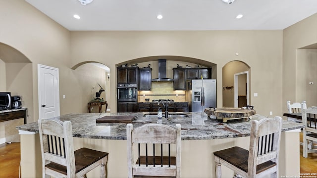 kitchen featuring wall chimney exhaust hood, a kitchen breakfast bar, a sink, and stainless steel fridge with ice dispenser