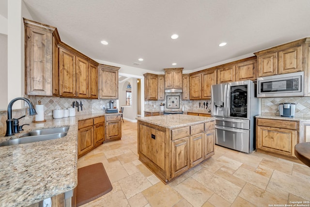 kitchen with light stone counters, stone tile floors, stainless steel appliances, a sink, and a kitchen island