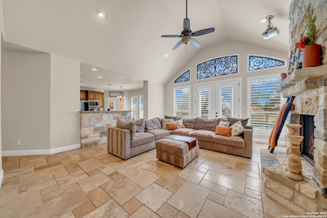 living room featuring stone tile floors, a wealth of natural light, a stone fireplace, high vaulted ceiling, and baseboards