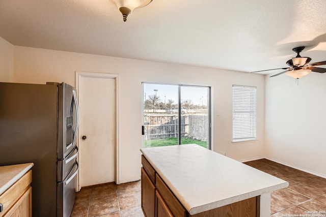 kitchen featuring brown cabinetry, a kitchen island, light countertops, stainless steel refrigerator with ice dispenser, and light tile patterned flooring