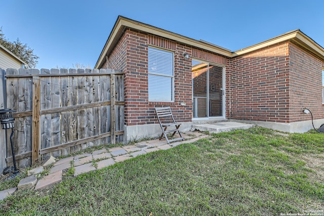 back of property featuring fence, a lawn, and brick siding