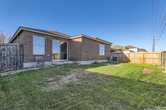 rear view of house featuring a yard, brick siding, a fenced backyard, and central air condition unit