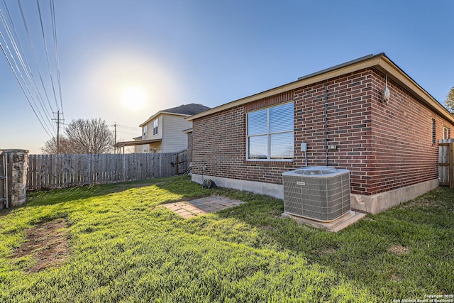 view of side of property featuring brick siding, a yard, fence, and central air condition unit