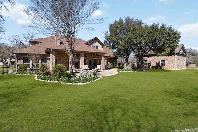 rear view of house featuring brick siding, a lawn, and fence