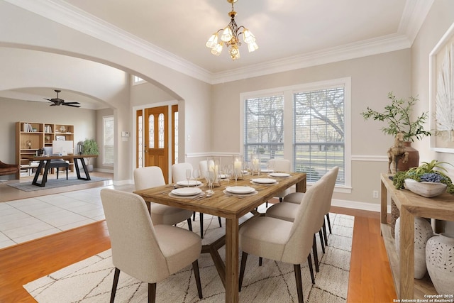 dining area featuring arched walkways, crown molding, baseboards, and light wood-style floors