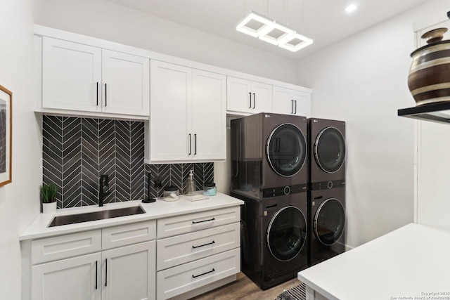 clothes washing area featuring stacked washer and dryer, wood finished floors, a sink, and cabinet space