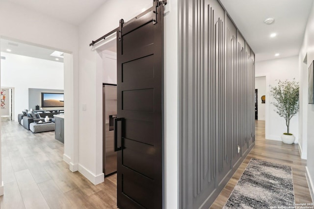 hall featuring light wood finished floors, a barn door, baseboards, and recessed lighting