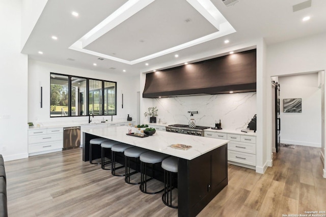 kitchen featuring a breakfast bar area, stove, a spacious island, wall chimney range hood, and dishwasher