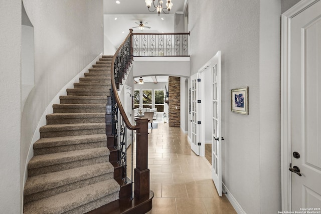 tiled entrance foyer featuring arched walkways, stairway, a high ceiling, baseboards, and ceiling fan with notable chandelier