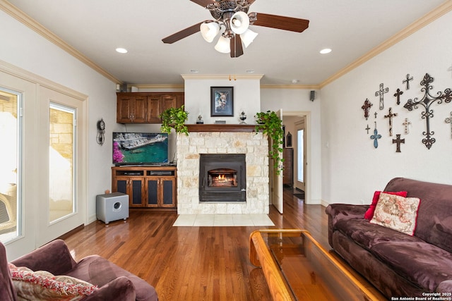 living room featuring a ceiling fan, wood finished floors, crown molding, a stone fireplace, and recessed lighting