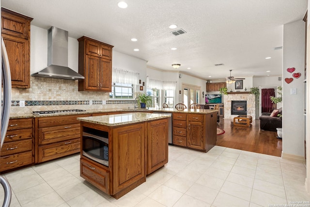 kitchen featuring tasteful backsplash, appliances with stainless steel finishes, open floor plan, a peninsula, and wall chimney exhaust hood