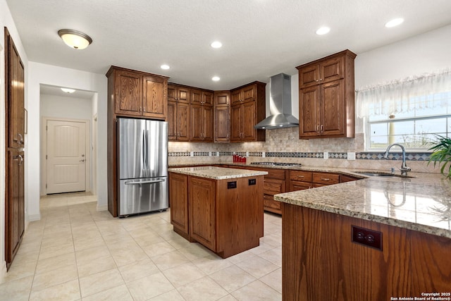 kitchen featuring tasteful backsplash, appliances with stainless steel finishes, light stone countertops, wall chimney range hood, and a sink