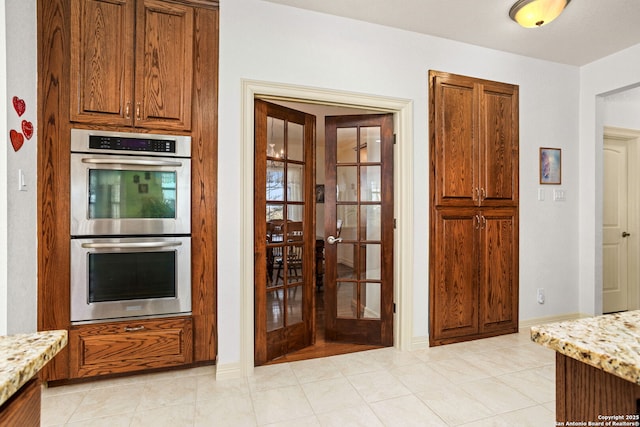 kitchen featuring double oven, light stone counters, light tile patterned flooring, french doors, and brown cabinets