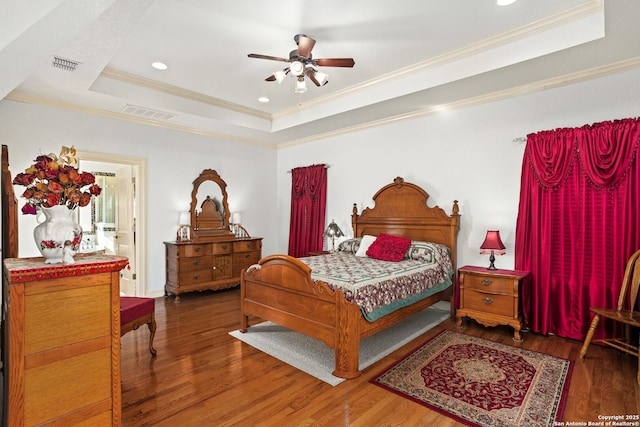 bedroom featuring visible vents, crown molding, a tray ceiling, and wood finished floors