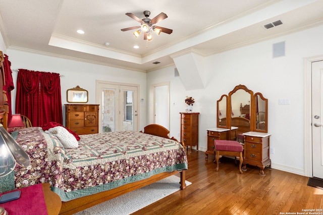 bedroom featuring visible vents, baseboards, ornamental molding, a tray ceiling, and hardwood / wood-style floors