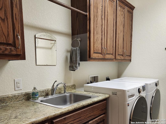 clothes washing area with a textured wall, separate washer and dryer, a sink, and cabinet space